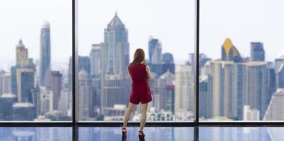 Luxury young Asian CEO woman entrepreneur looking at the downtown skyline at the window with skyscraper and cityscape for vision and real estate development photo