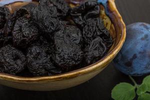 Dried plums in a bowl on wooden background photo