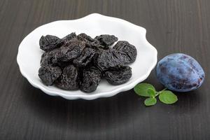 Dried plums in a bowl on wooden background photo