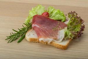 Sándwich de prosciutto sobre tablero de madera y fondo de madera foto