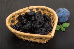 Dried plums in a basket on wooden background photo