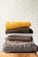 Stack of autumn warm sweaters on modern coffee table, white brick wall background photo