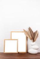 White frames mockup with dry palm leaves in a vase on wooden table photo