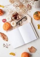 libro blanco en blanco con hojas de otoño, vasos y velas en mesa blanca, diseño de maqueta foto