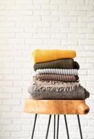 Stack of autumn warm sweaters on modern coffee table, white brick wall background photo