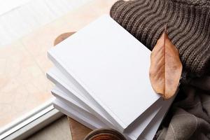 Stack of white blank books with autumn leaves and cup of hot tea on old wooden chair, mockup design photo