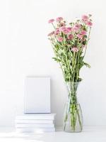 maqueta de libro blanco con flores de crisantemo en un jarrón sobre una mesa blanca foto