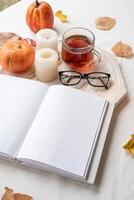 white blank book with autumn leaves, glasses and candles on white table , mockup design