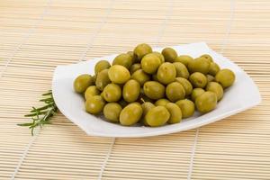 Green olives on the plate and wooden background photo