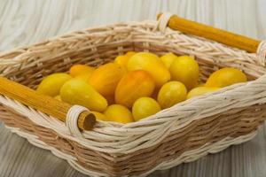 Yellow cherry tomatoes in a basket on wooden background photo