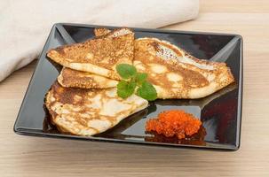 Pancakes with red caviar on the plate and wooden background photo