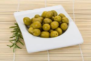 Green olives in a bowl on wooden background photo