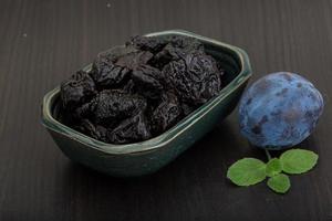 Dried plums in a bowl on wooden background photo