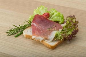 Prosciutto sandwich on wooden board and wooden background photo