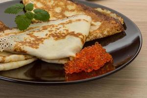 Pancakes with red caviar on the plate and wooden background photo