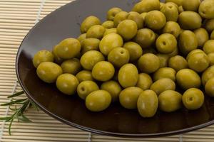 Green olives on the plate and wooden background photo