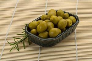 Green olives in a bowl on wooden background photo