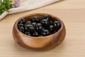 Black olives in a bowl on wooden background photo
