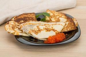 Pancakes with red caviar on the plate and wooden background photo