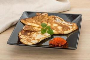 Pancakes with red caviar on the plate and wooden background photo