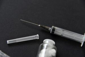 An empty medical syringe and a glass bottle on a black background. photo