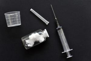 An empty medical syringe and a glass bottle on a black background. photo