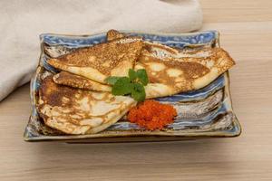 Pancakes with red caviar on the plate and wooden background photo