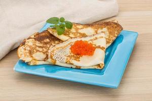 Pancakes with red caviar on the plate and wooden background photo