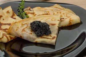 tortitas con caviar negro en el plato y fondo de madera foto