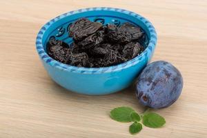 Dried plums in a bowl on wooden background photo