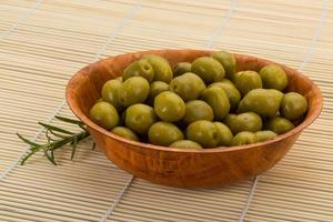 Green olives in a bowl on wooden background photo