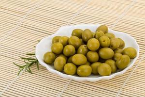 Green olives on the plate and wooden background photo