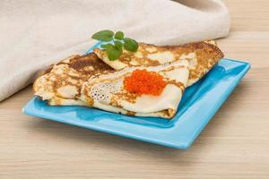 Pancakes with red caviar on the plate and wooden background photo