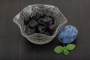 Dried plums in a bowl on wooden background photo