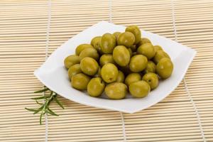 Green olives on the plate and wooden background photo