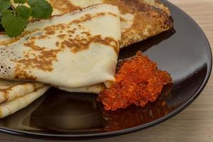 Pancakes with red caviar on the plate and wooden background photo