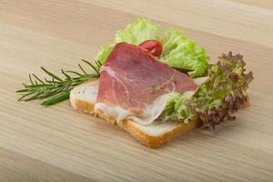 Prosciutto sandwich on wooden board and wooden background photo