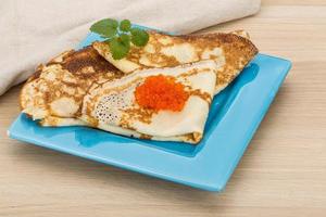 Pancakes with red caviar on the plate and wooden background photo