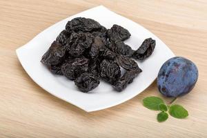 Dried plums in a bowl on wooden background photo