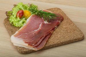 Prosciutto on wooden board and wooden background photo