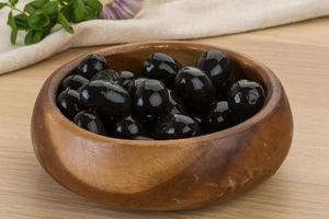 Black olives in a bowl on wooden background photo