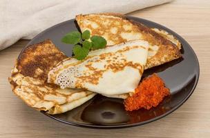 Pancakes with red caviar on the plate and wooden background photo