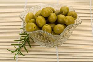 Green olives in a bowl on wooden background photo