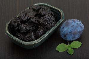 Dried plums in a bowl on wooden background photo