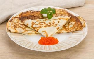 Pancakes with red caviar on the plate and wooden background photo