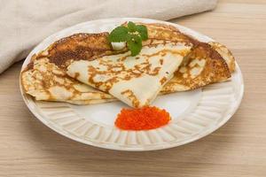 Pancakes with red caviar on the plate and wooden background photo