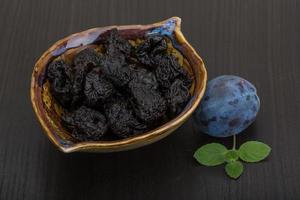 Dried plums in a bowl on wooden background photo