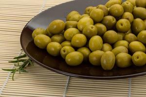 Green olives on the plate and wooden background photo
