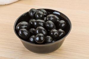 Black olives in a bowl on wooden background photo