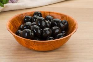 Black olives in a bowl on wooden background photo